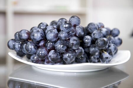 White Porcelain Plate of Purple Grapes on Reflective Tableの写真素材