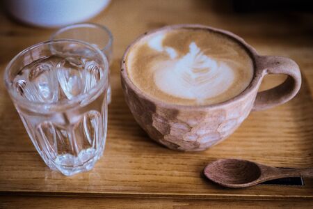 Cup of cappuccino with latte art on Wooden plate ,Glass of water, glass of syrup.の写真素材