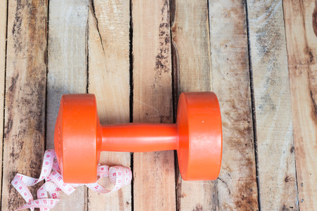 Orange dumbbells and measuring tape  on  wood background.の写真素材