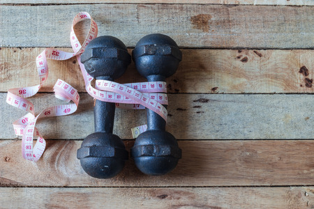 Old dumbbells with  measuring tape on wooden backgroundの写真素材