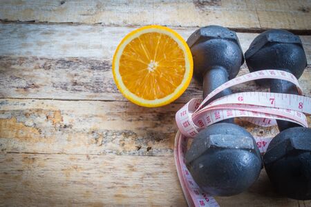 Old dumbbells with measuring tape on wooden background. Diet conceptの写真素材