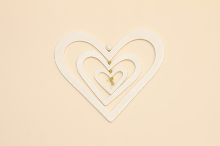 A three layer white heart made of wood hanging on a cream wall centered in the photoの写真素材