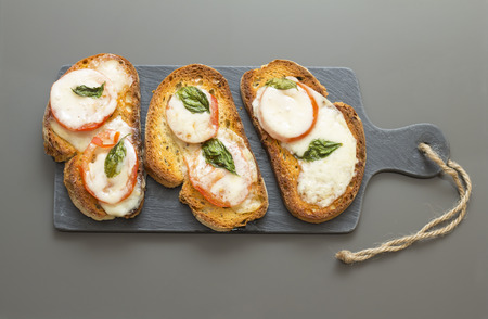 Three Beautifull and delicious italian style charcoal grilled bruschetta with tomato cheese and basil, over a slate dish isolated in a grey background.の写真素材
