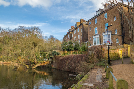 Luxury typical brick british houses with gardens in front of a lake with a fallen tree into the...