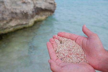 Man holding on his hands a bunch of beach sand in tones of pink with the sea as backgroundの写真素材