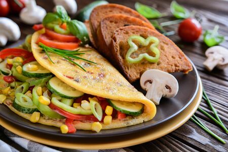 Omelet with pepper, tomato, corn, green onion, cucumber, mushrooms and fried bread on a wooden backgroundの写真素材
