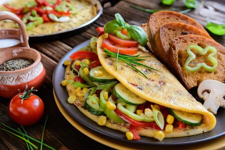 Omelet with pepper, tomato, corn, green onion, cucumber, mushrooms and fried bread on a wooden backgroundの写真素材