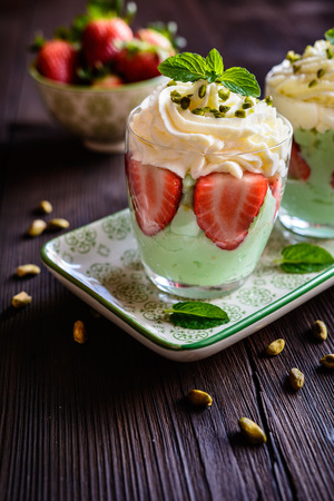 Delicious pistachio pudding with strawberries and whipped cream in a glass jarの写真素材