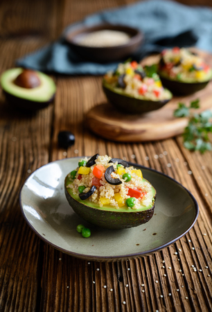 Avocado stuffed with quinoa, green peas, tomato, olives, red and yellow bell pepper and parsleyの写真素材