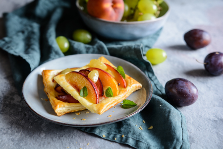 Fruit puff pastry pies with sliced peach, plums and grapesの写真素材
