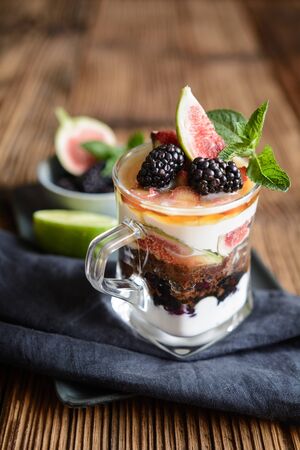 Sweet dessert with Ricotta cheese, crushed cookies, rhubarb, figs, topped with maple syrup in a jarの写真素材