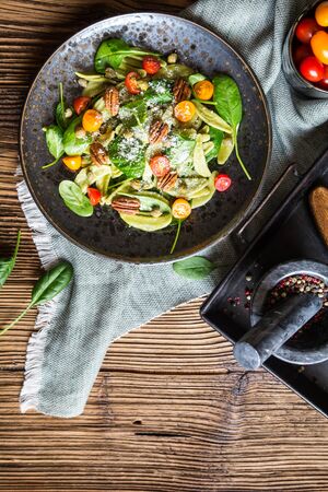 Vegetarian pasta salad with spinach, red and orange tomato, capers and pecan nuts, topped with shredded cheese on ceramic plateの写真素材
