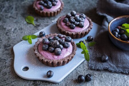 Chocolate tartlets filled with blueberry mascarpone cream topped with blueberries and powdered sugarの写真素材