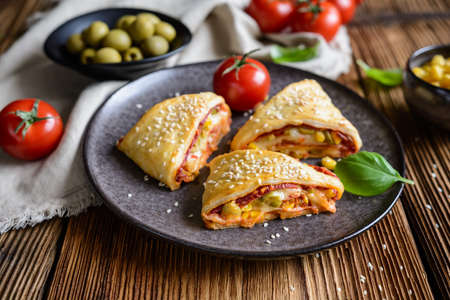 Delicious puff pastry pizza triangle rolls stuffed with tomato sauce, ham, cheese, corn, olives and...