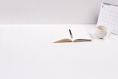White office desk table with notepad, coffee cup and calendar.