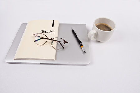 Notebook with a cup of coffee and glasses on a white backgroundの写真素材