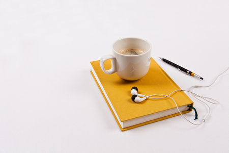 A cup of coffee with headphones and a book on a white backgroundの写真素材