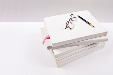 Stack of books with eyeglasses and pen on white background.の写真素材