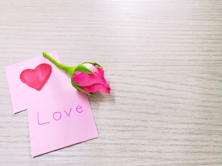 Beautiful pink rose flower with pink paper (write love and heart) on a wooden backgroundの写真素材