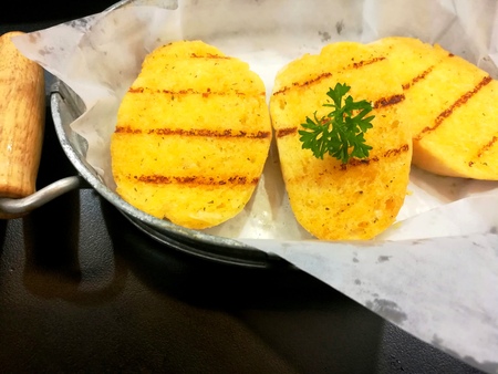 Delicious garlic bread on paper in aluminum tray placed on black table