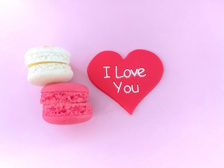 Delicious colorful macarons are stacked with red heart are beautiful on pink background