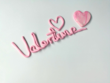 Valentine's text and sweet pink heart are handmade from plasticine clay, placed on a white...