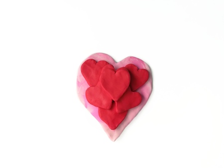 Beautiful several red hearts are placed on a pink heart handmade from plasticine clay are on white...