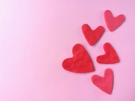 Many red heart made from plasticine clay on pink background, cute shaped dough
