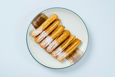 Chocolate churos with powdered sugar topping served on a white plate.の写真素材