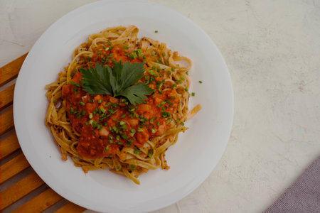 flat lay of a plate of spaghetti topped with tomato sauce mixed with meat, cheese, spices, onions stands on a wooden tray.の写真素材