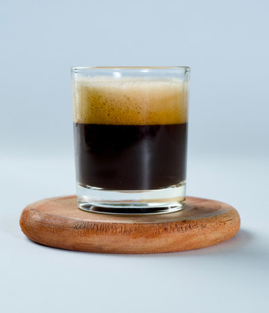 a 60 ml glass of espresso standing on a glass tray made of woodの写真素材