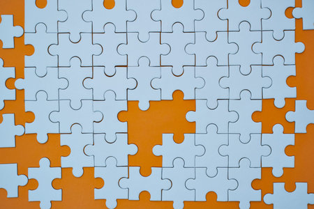 Incomplete white jigsaw puzzle pieces rest upon a vibrant, textured orange background surface.の写真素材
