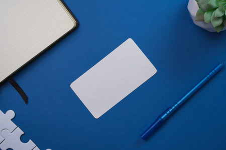 Organized workspace flat lay shows a blank white card, dotted notebook, and blue pen.の写真素材