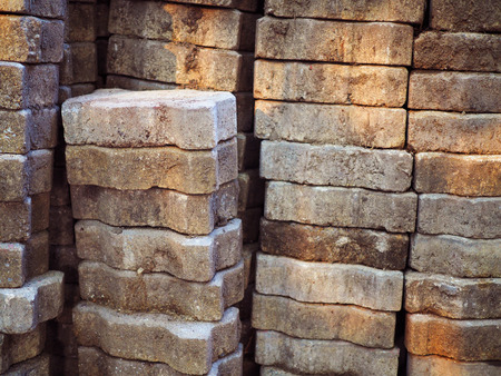 Side view of stacked grainy texture worm zigzag jigsaw shape concrete block brick pile, under warm yellow sunlight shade reflection backgroundの写真素材