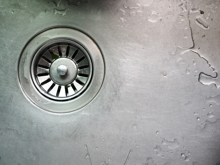Grey shiny scratch stainless steel wet basin kitchen sink with draining hole mesh, water, food trash remain backgroundの写真素材