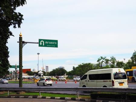 BANGKOK, THAILAND - SEPTEMBER 25, 2017: Green traffic direction sign to "Sanum Luang" on royal style traditional decorated pole, on Rajchadamneon road, green tree bush middle islands, cars drivingのeditorial素材