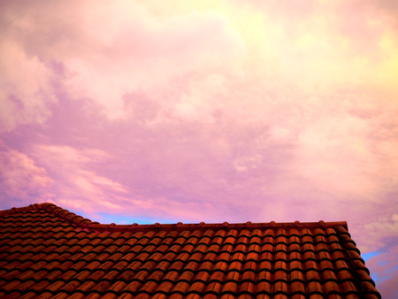 Red yellow sunlight reflecting cloudy sky in the morning, with dark orange concrete slope roof backgroundの写真素材