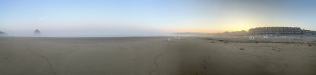 Panorama of the beach at sunrise with fog and rocks in the backgroundの素材
