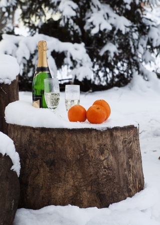 Bottle of champagne, glasses, oranges on to snow in the forest before New Yearの写真素材
