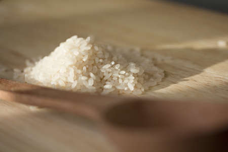 Rice grains and empty wooden spoon. Sunbeams and shade. の写真素材