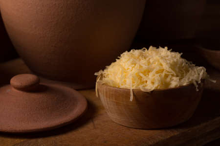 Grated cheese in a wooden bowl on the kitchen tableの写真素材
