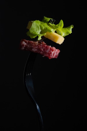 Salami, cheese and lettuce on a fork, dark backgroundの写真素材