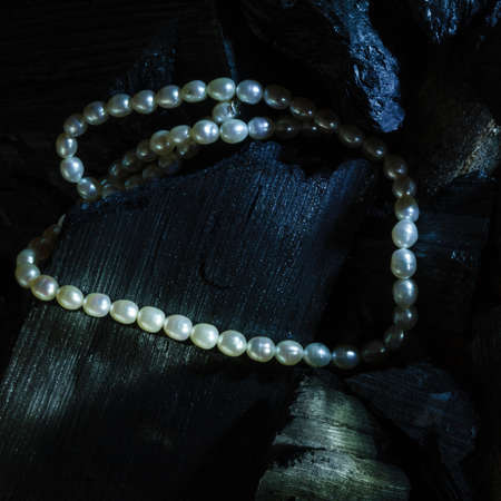 Pearl necklace on black coals with glare lightの写真素材