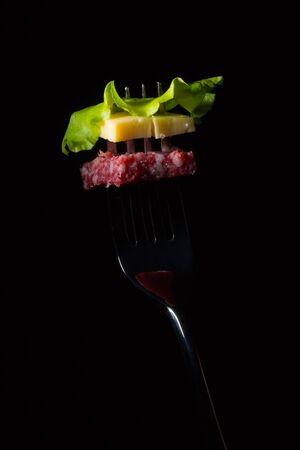 Salami, cheese and lettuce on a fork, dark backgroundの写真素材