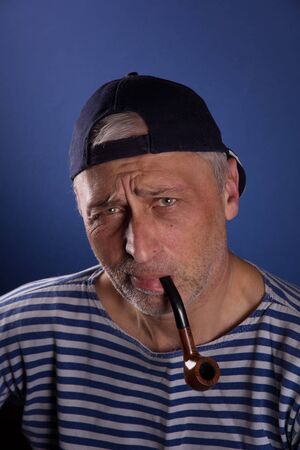 Man in striped clothing smoking a pipe and looking at camera while standing against blue backgroundの写真素材