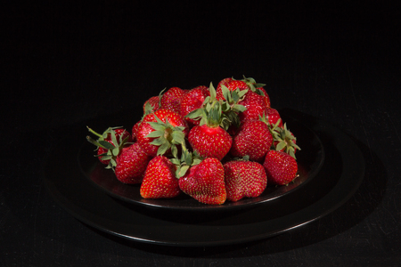 Fresh ripe strawberry in a black plate on a dark backgroundの写真素材