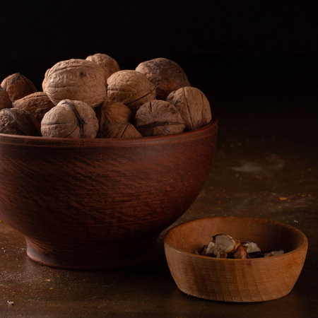 Whole and peeled walnuts in ceramic and wooden dishes on a dark backgroundの写真素材