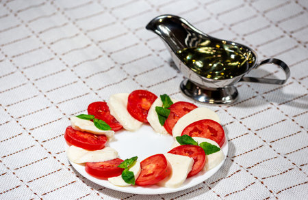 Caprese - mozzarella, tomato, green basil on a white plate with gravy on a clothの写真素材