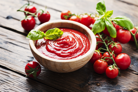 Bowl of tomato sauce and cherry tomatoes on the wooden table, selective focusの写真素材