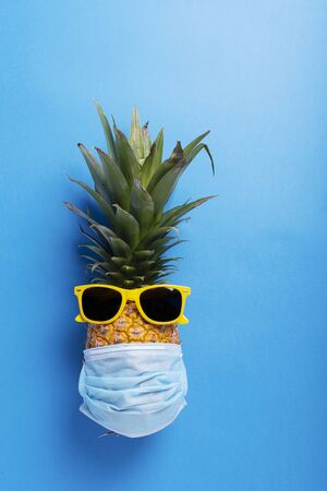 Concept of summer vacation 2020. Pine apple with a medical mask and sun glasses on the blue background. Top view imageの写真素材